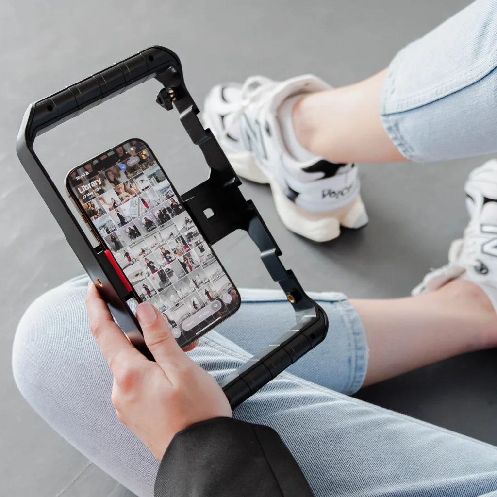 Ujęcie nóg kobiety w jeansach i sportowych butach. Trzyma w dłoniach telefon w obudowie do nagrywania reelsów.